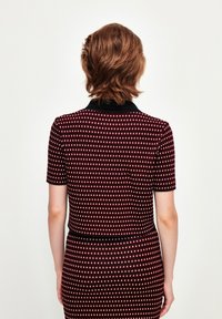 Robe ajustée jusqu'au genou avec des manches courtes, col noir, fond bordeaux et motif en losanges blancs. Surface texturée, design minimaliste.