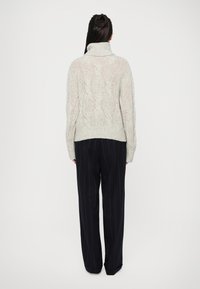 Pull en tricot gris clair avec un col montant, présentant un motif de tricot en câble. Associé à un pantalon large à rayures verticales navy foncé.