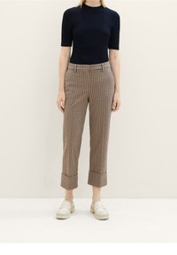 Haut côtelé à manches courtes bleu marine associé à un pantalon court à motif écossais marron. Des mocassins à plateforme de couleur claire complètent le look.