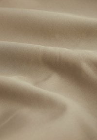 Beige kangas, joka on sileä, esittää pehmeitä laskoksia ja hienovaraista kiiltoa. Kevyt materiaali, jossa on tasainen, hieno kudos.