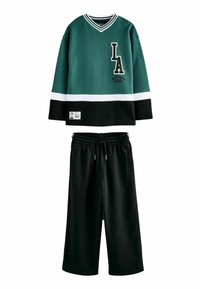 Grünes und schwarzes, strukturiertes Langarmoberteil mit weißen Streifen und "LA"-Logo, kombiniert mit schwarzen cropped Pants mit elastischem Bund.