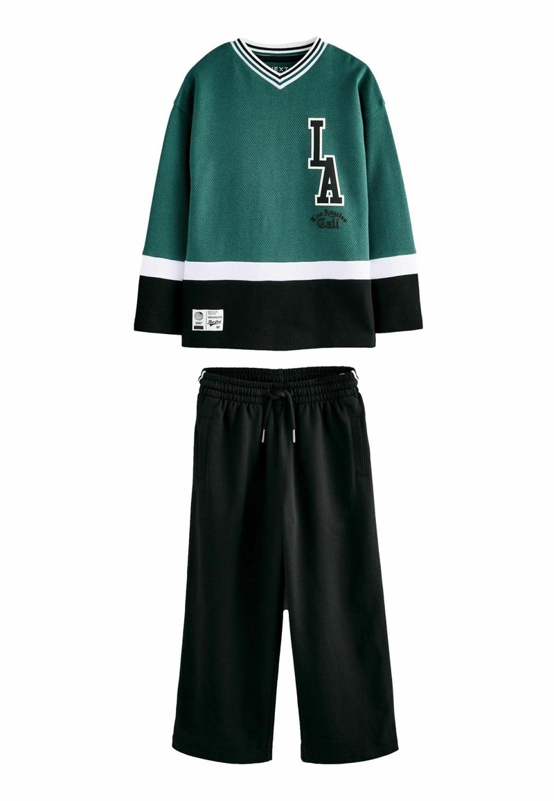 Grünes und schwarzes, strukturiertes Langarmoberteil mit weißen Streifen und "LA"-Logo, kombiniert mit schwarzen cropped Pants mit elastischem Bund.