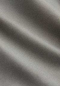Szary materiał o gładkiej, teksturowanej powierzchni i subtelnym połysku, z delikatnymi, równymi liniami tworzącymi miękki, falisty wzór.