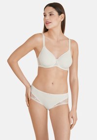 Set di reggiseno e slip beige realizzato in tessuto morbido con accenti di pizzo. Il reggiseno presenta coppe lisce e spalline regolabili; gli slip hanno lati testurizzati.