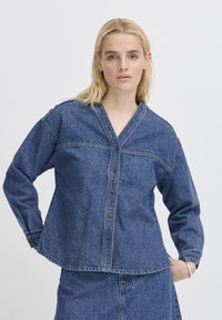 Denimskjorta med V-ringning, knäppning fram, långa ärmar och sydda sömmar. Har en avslappnad passform och bleknar i en mellanblå nyans.