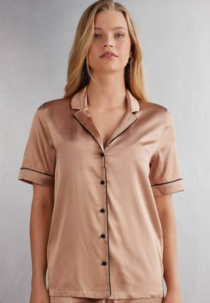 Korte mouwen zijden pyjama top in licht beige met zwarte piping, een gesneden kraag en een sluiting met knopen aan de voorkant. Gladde textuur en een ontspannen pasvorm.
