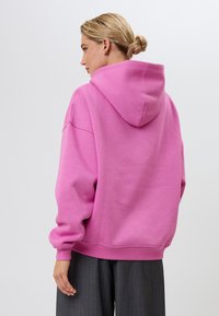 Pārmēra rozā sporta kapuce ar auklu, ribota apkakle un apakšmala, izgatavota no mīksta kokvilnas maisījuma, ar brīvu siluetu.