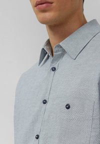 Lichtblauw overhemd met knoopsluiting en een gestructureerde stof, voorzien van een spitse kraag, donkerblauwe knopen en een borstzak.