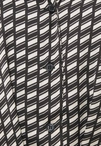 Svart- och vitmönstrad blus med diagonala ränder, med en slät textur och svarta knappar framtill.