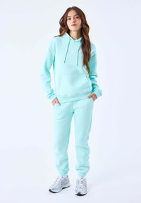 Sudadera verde menta con un bolsillo frontal y cordones, combinada con joggers ajustados a juego. Presenta un sutil bordado de logo y una textura suave.