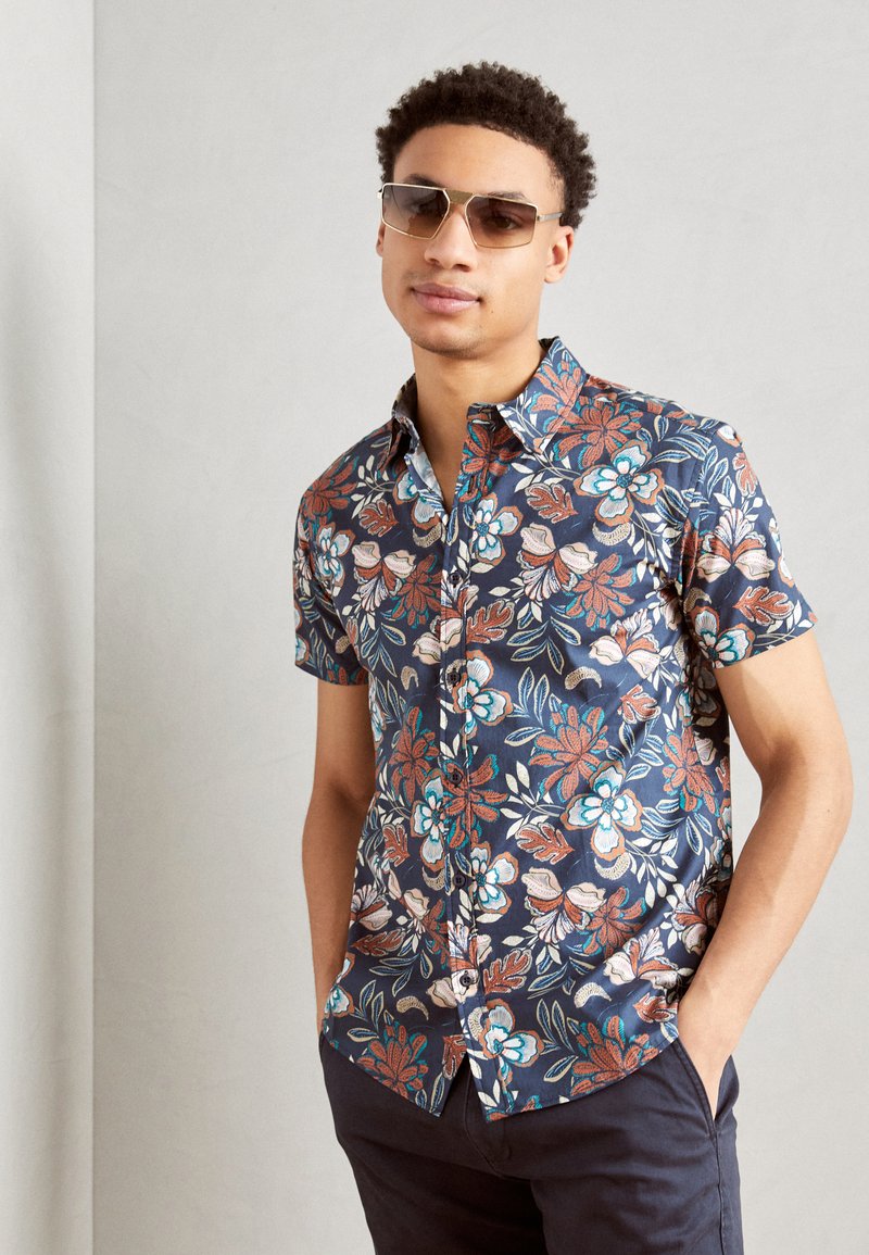 Kortærmet skjorte med knapper i marineblå med farverigt blomstermotiv. Har en klassisk krave, struktureret stof og slim fit-design.