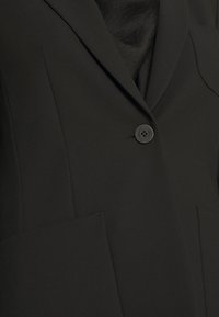 Černý blazer se zapínáním na jedno knoflíkové, ostrými klopami a dvěma předními kapsami s hladkým povrchem látky.