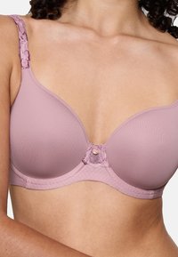 Světlé růžové podprsenka s vycpávkami a krajkovými ramínky, dekorativním středovým panelem a hladkým povrchem, nabízející bezproblémový vzhled a pohodlné nošení.