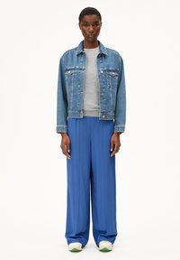 Denim jacket in light blue, gray sweatshirt underneath, wide-leg blue pants, white sneakers with green accents. Simple design, relaxed fit.