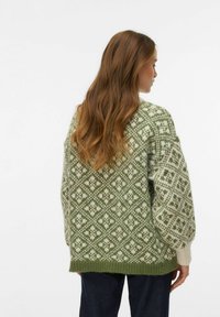 Pull vert et ivoire à motifs, coupe ample, texture en maille, et poignets côtelés. Présente un motif de losanges et de fleurs sur toute la surface.