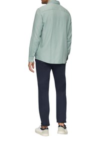 Lichtgroen, langemouwen shirt van zachte stof met een achterste halsnaad; gecombineerd met donkerblauwe slim-fit trousers en witte sneakers.