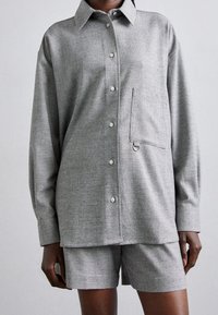 Chemise grise à boutons avec une poche poitrine mettant en avant un détail en anneau métallique, assortie de shorts gris fabriqués dans un tissu texturé.
