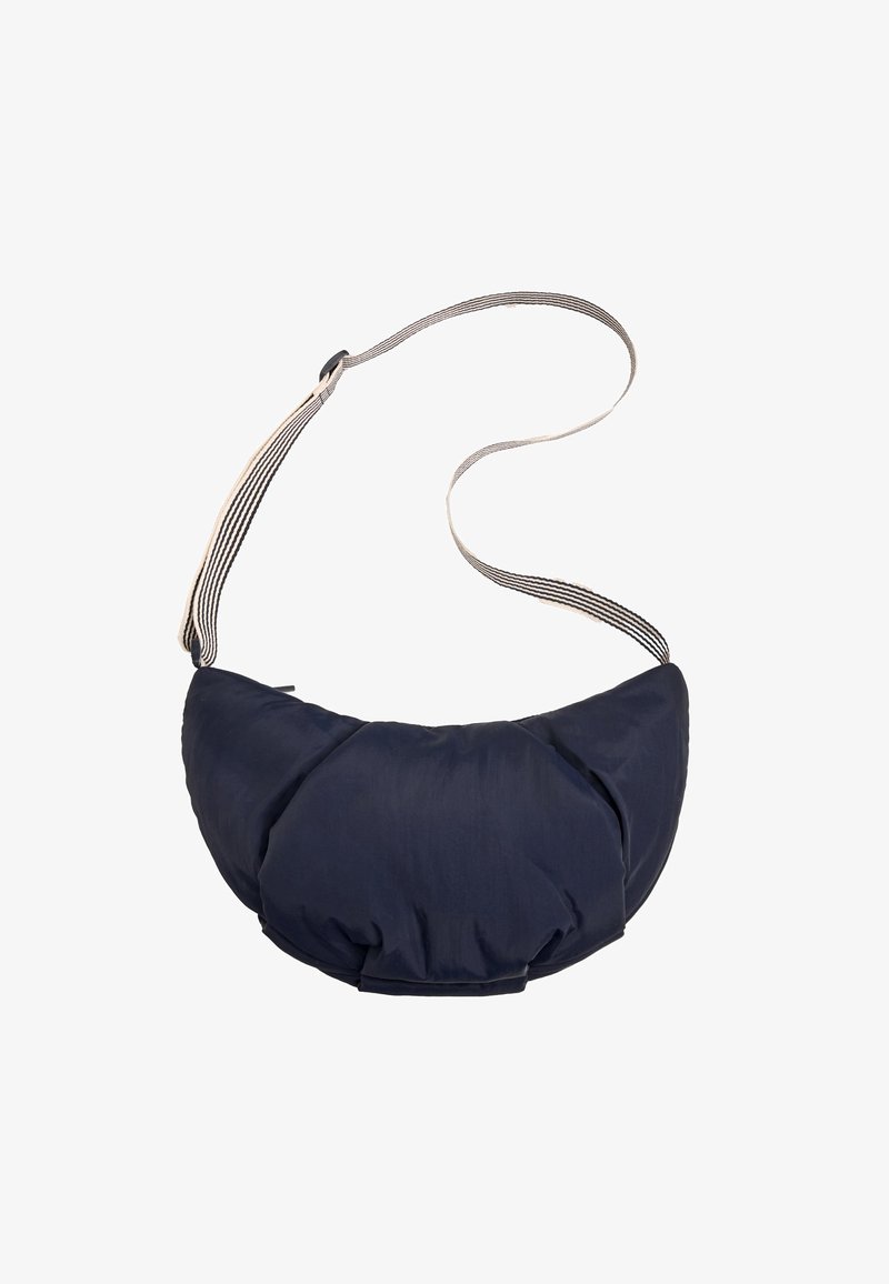Sac bandoulière matelassé forme croissant bleu marine avec sangle ajustable rayée noir et blanc sur fond blanc.