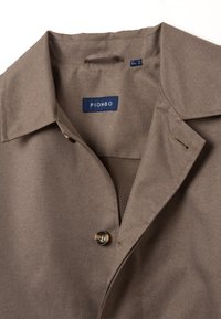 Giacca marrone con colletto classico, chiusura a bottoni e fodera in rete. L'etichetta riporta "PIOMBO." Il tessuto presenta una finitura testurizzata.
