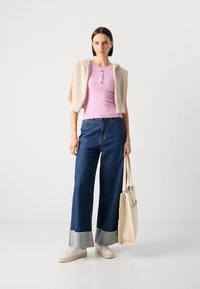 Lys rosa ribbet topp med tre knapper, sammen med brede blå jeans med et lett denimoppbrett, og hvite sneakers. Kremfarget tote bag holdt.