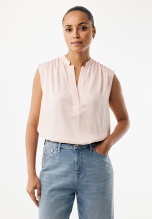 Ärmellose rosa Bluse mit einem v-förmigen Ausschnitt ohne Knöpfe und gerafften Details an den Schultern, kombiniert mit hellblauen, hoch taillierten Jeans.