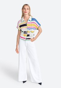 Chandail en crochet à manches courtes avec des rayures multicolores, présentant un col blanc, des accents verts et des boutons sur le devant, associé à un pantalon large blanc.