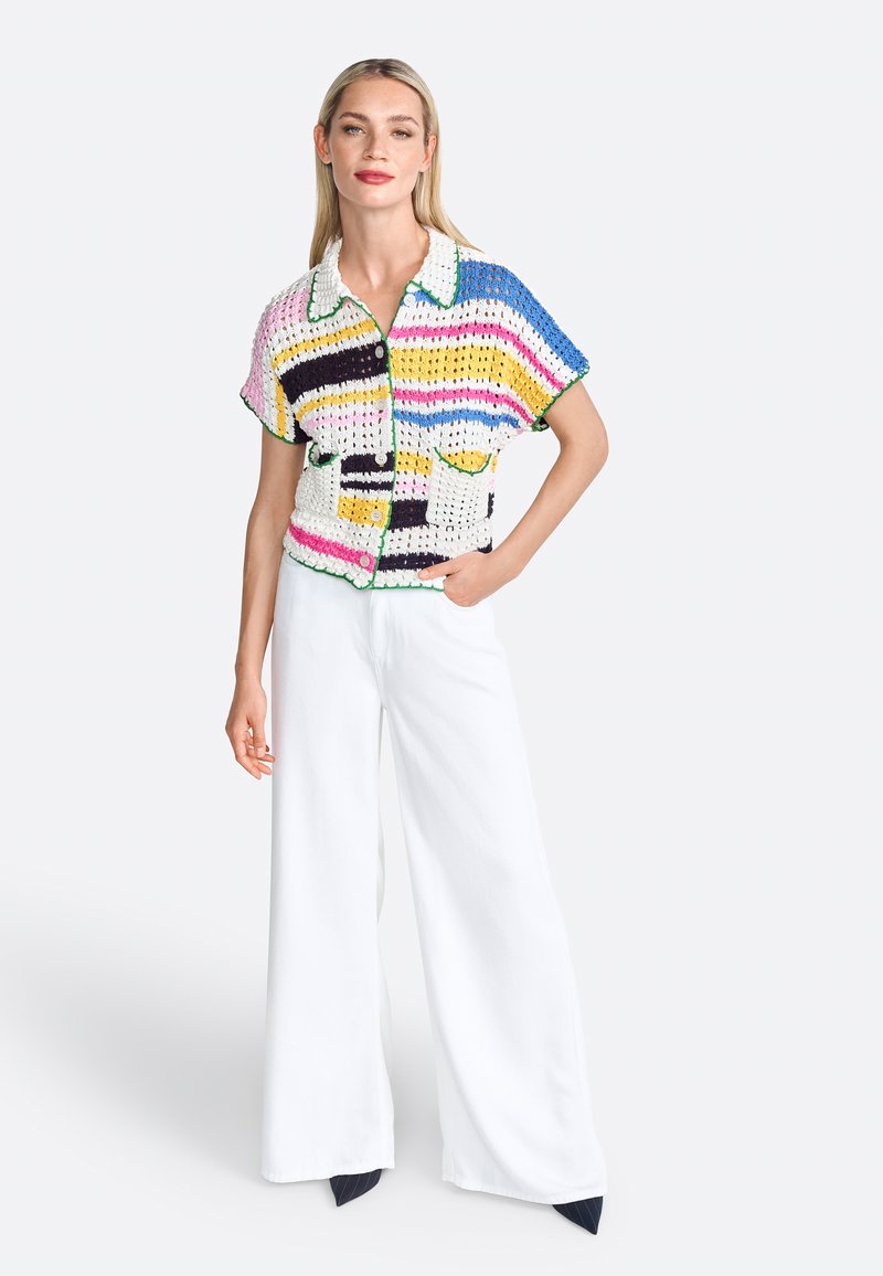 Chandail en crochet à manches courtes avec des rayures multicolores, présentant un col blanc, des accents verts et des boutons sur le devant, associé à un pantalon large blanc.