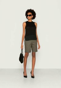 Top preto sem mangas, calções verde-oliva, mala preta e sapatos de salto alto. Tecido suave com uma bainha em camadas no topo.