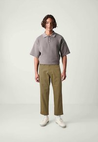 Γκρι κοντομάνικο πόλο με υφασμάτινη υφή, γιακάς με τρία κουμπιά. Παντελόνι χακί με ίσια κοπή, συνδυασμένο με λευκά αθλητικά παπούτσια.