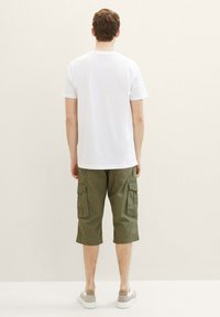 Weißes T-Shirt mit kurzen Ärmeln kombiniert mit olivgrünen Cargo-Shorts mit Seitentaschen, ergänzt durch hellfarbige Sneakers.
