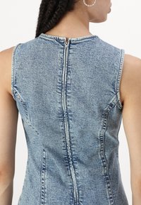 Vestido de ganga com design sem mangas, na cor azul clara, e um zíper na parte de trás. Tecido texturizado com costuras e detalhes visíveis.