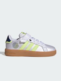 Λευκό sneaker Adidas με φλούο κίτρινες ρίγες, λαστιχένια σόλα, μαύρο λογότυπο στη φτέρνα και λουράκι με βέλκρο πάνω από τα κορδόνια, πλευρική όψη σε μονόχρωμο φόντο.