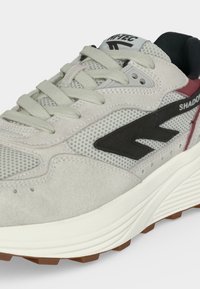 Ανοιχτό γκρι δερμάτινο και υφασμάτινο αθλητικό παπούτσι με μαύρο λογότυπο, λευκή σόλα και μπεζ κορδόνια, που δείχνει λεπτομέρειες από μπροστά και πλάι.