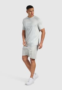 Camiseta atlética gris claro de manga corta, con un diseño de logo sutil. Combinada con pantalones cortos gris claro y zapatillas blancas.