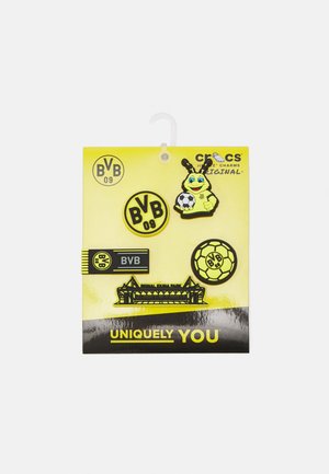 Ensemble de cinq charms en caoutchouc sur un fond jaune, avec des logos BVB noirs et jaunes, une abeille de dessin animé tenant un ballon de football, et une silhouette de stade.