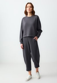 Felpa grigia cropped con maniche lunghe, abbinata a joggers tapered coordinati. Entrambi realizzati in morbido tessuto, con tasche laterali e una vestibilità rilassata.