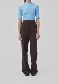 Top blu corto a maniche corte abbinato a pantaloni marroni a gamba larga e vita alta. I pantaloni hanno una chiusura frontale con bottone e una consistenza liscia. Scarpe nere.