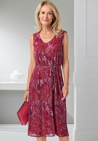 Ärmelloses Kleid mit Floral-Muster in Rot- und Violetttönen, mit V-Ausschnitt und gebundenem Taillenband. Glatte, fließende Stoffqualität. Ergänzt durch eine pinkfarbene Clutch.