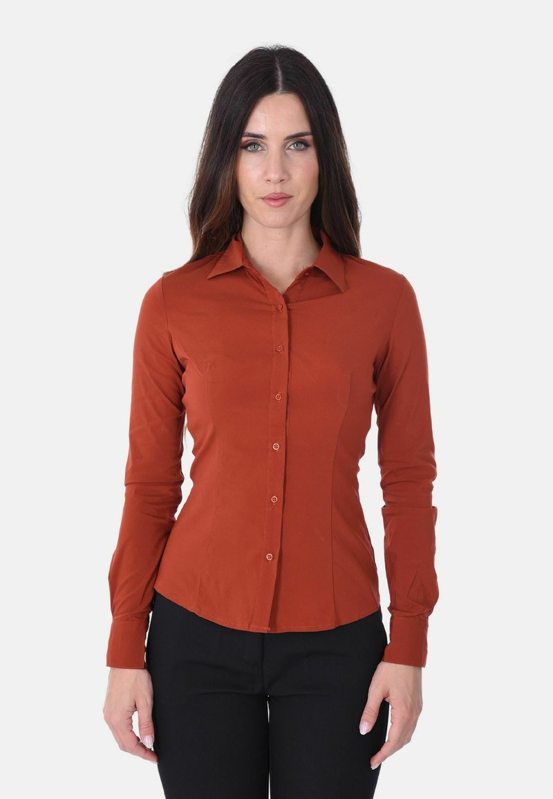 Camicia button-up di colore ruggine con maniche lunghe, design aderente, colletto e tasche frontali visibili. Il tessuto appare liscio senza motivi.