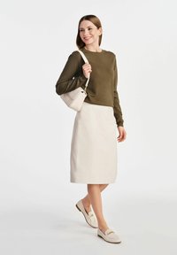 Oliwkowy sweter z długim rękawem, kremowa spódnica oł�ówkowa, jasnobeżowa torebka na ramię i beżowe mokasyny z złotymi akcentami.