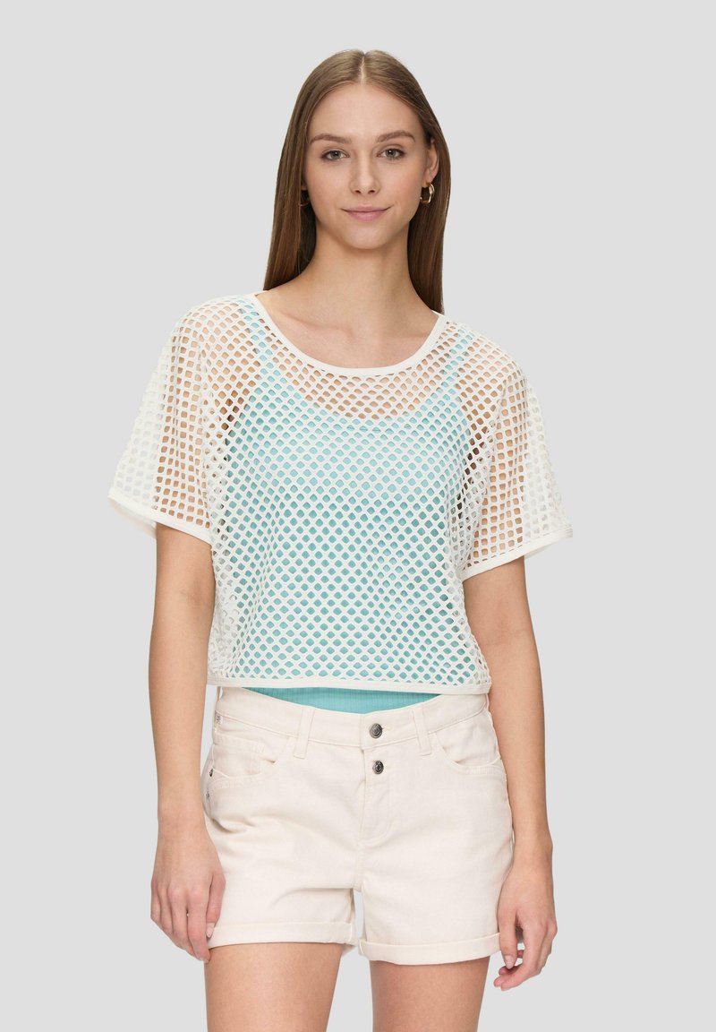 Geknipte mesh top met wit ruitpatroon; blauwe binnenlaag, korte mouwen, ronde hals; gecombineerd met lichtbeige shorts.