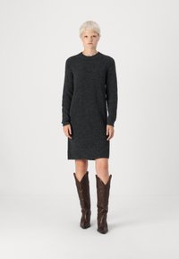 Φόρεμα-πουλόβερ από σκούρο γκρι πλεκτό υλικό, με μακριά μανίκια, στρογγυλή λαιμόκοψη και στρίφωμα λίγο πάνω από το γόνατο, συνδυασμένο με καφέ μπότες καουμπόη.