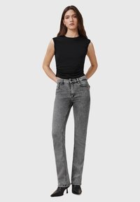 Top senza maniche nero abbinato a jeans in denim grigi a vita alta. I jeans presentano una texture leggermente sbiadita e dettagli di cucitura sottili.