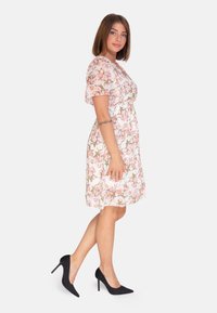 Blumenmusterkleid mit kurzen Ärmeln, rosa- und cremefarbenem Muster, tailliert, knielang, kombiniert mit schwarzen Stilettos.