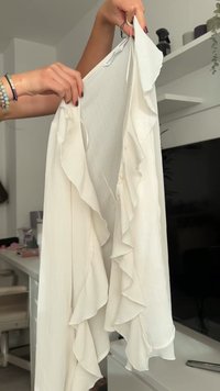 Blouse blanche en tissu léger, avec des bords froncés, des rayures verticales et trois boutons sur le devant.