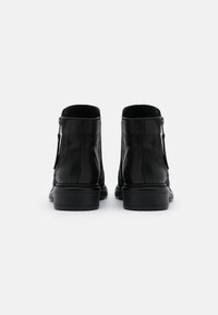 Botas de cuero negras hasta el tobillo con una textura suave, que cuentan con un cierre lateral y punta redonda, montadas sobre una suela negra resistente.