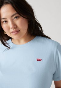 T-shirt en coton bleu clair avec un col rond et des manches courtes, orné d'un petit patch logo Levi's rouge sur la poitrine.