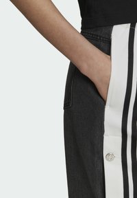 Svarta denimbyxor med en vit sidpanel som har horisontella svarta ränder, prydda med en silverknappdetalj vid midjan.