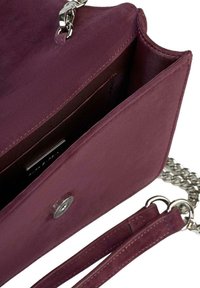 Zamszowa torebka w kolorze bordowym z srebrnym łańcuszkowym paskiem, srebrnym zatrzaskiem i kieszeniami wewnętrznymi. Tekstura jest miękka o gładkim wykończeniu.