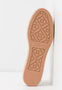 Semelle de chaussure en caoutchouc beige clair avec un motif floral, surface texturée pour une meilleure adhérence et une forme de orteil arrondie.